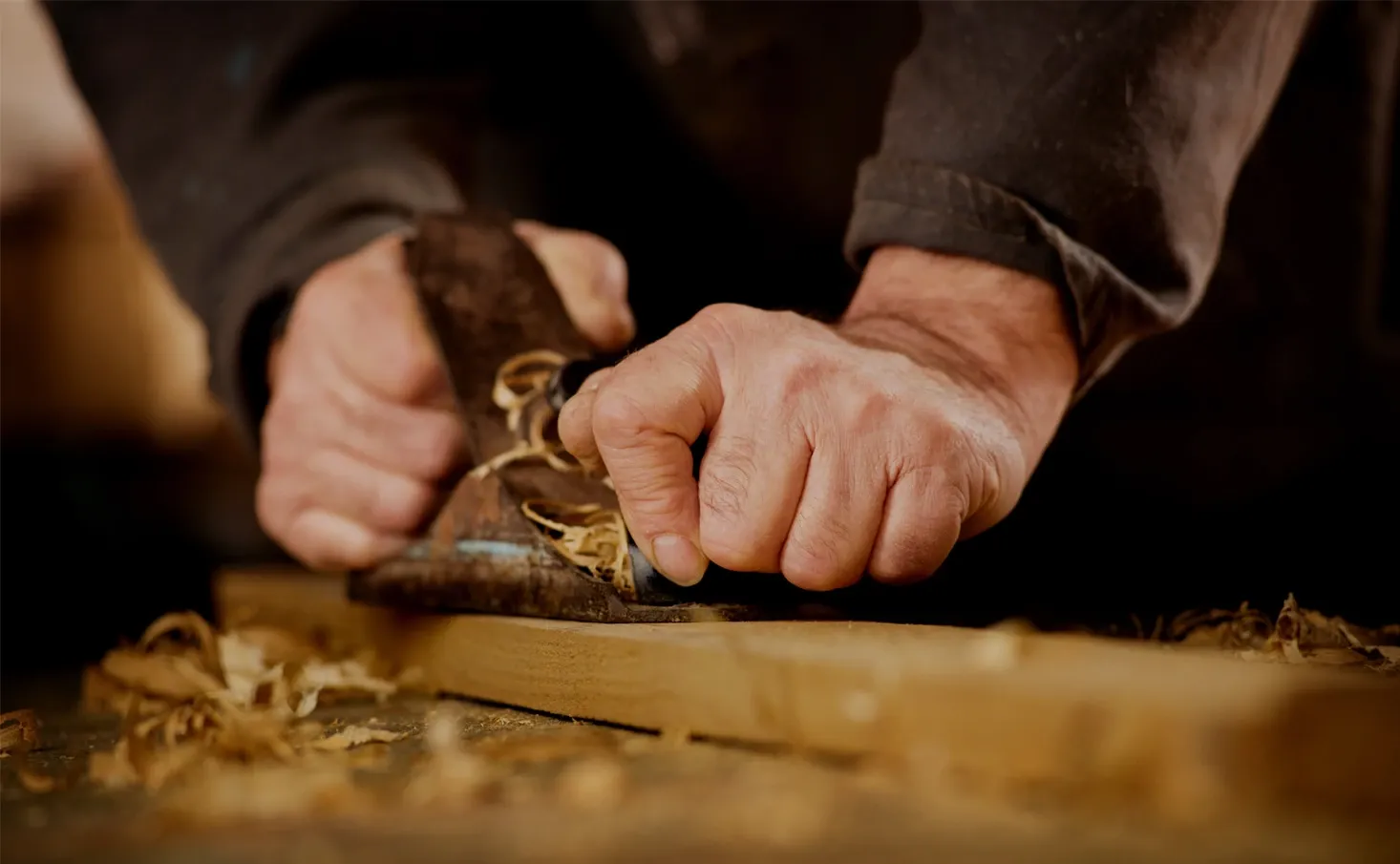 Hands guiding a hand plane across a piece of timber.